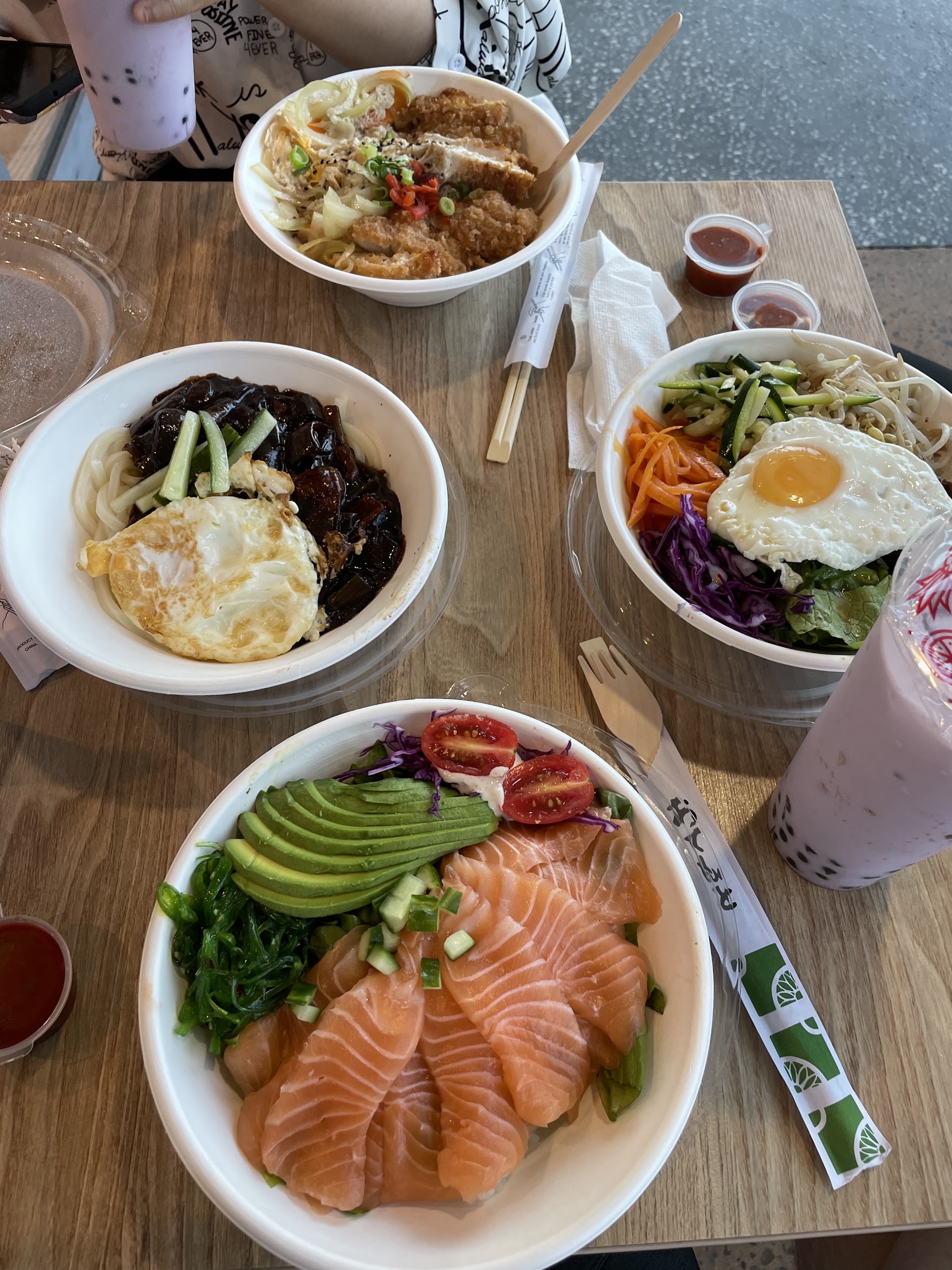 A table spread of katsudon, black bean noodles, bibimbap, salmon sashimi don and bubble tea