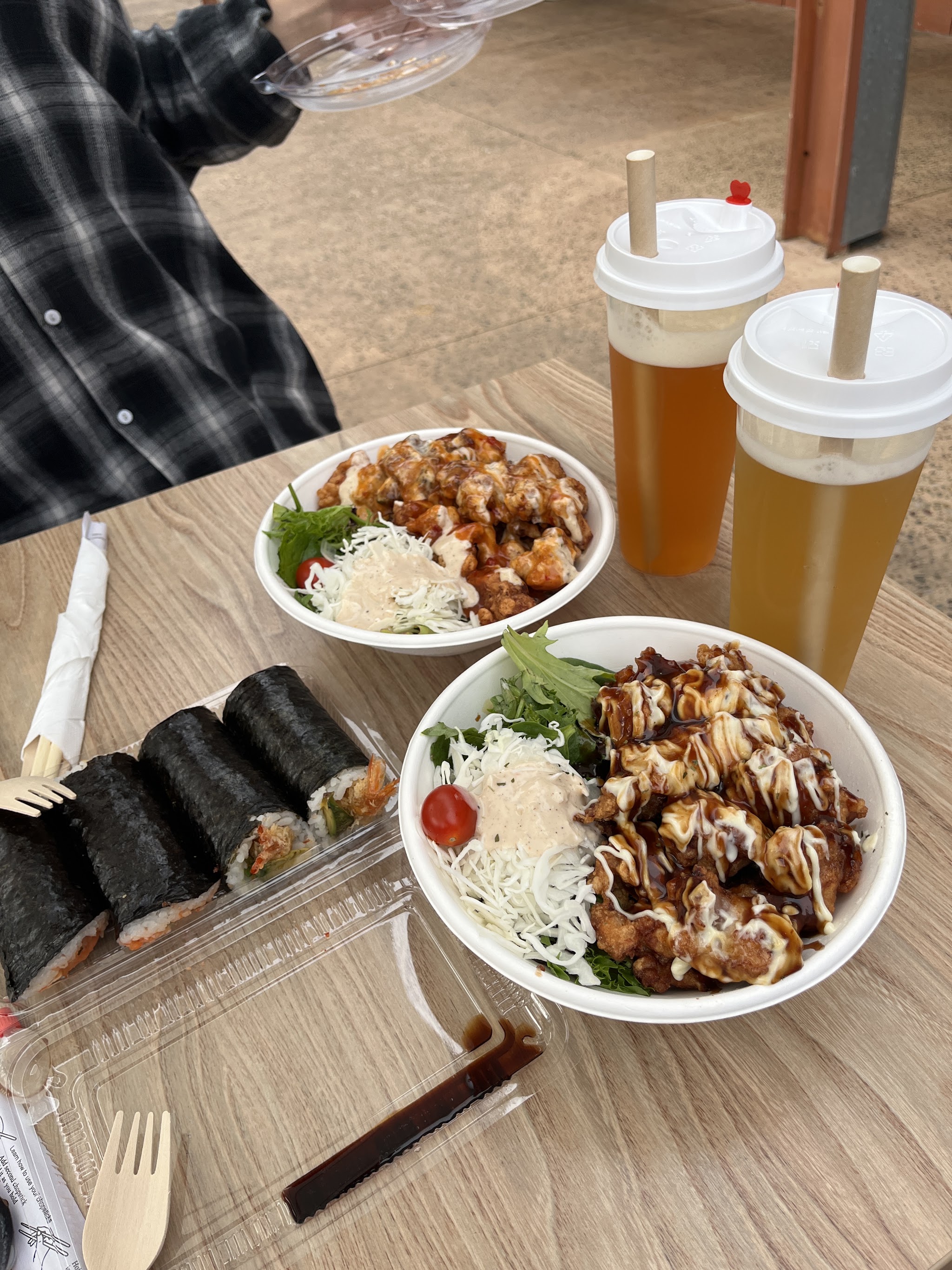Hand rolls, chicken rice bowls and two fruit teas on an outdoor table